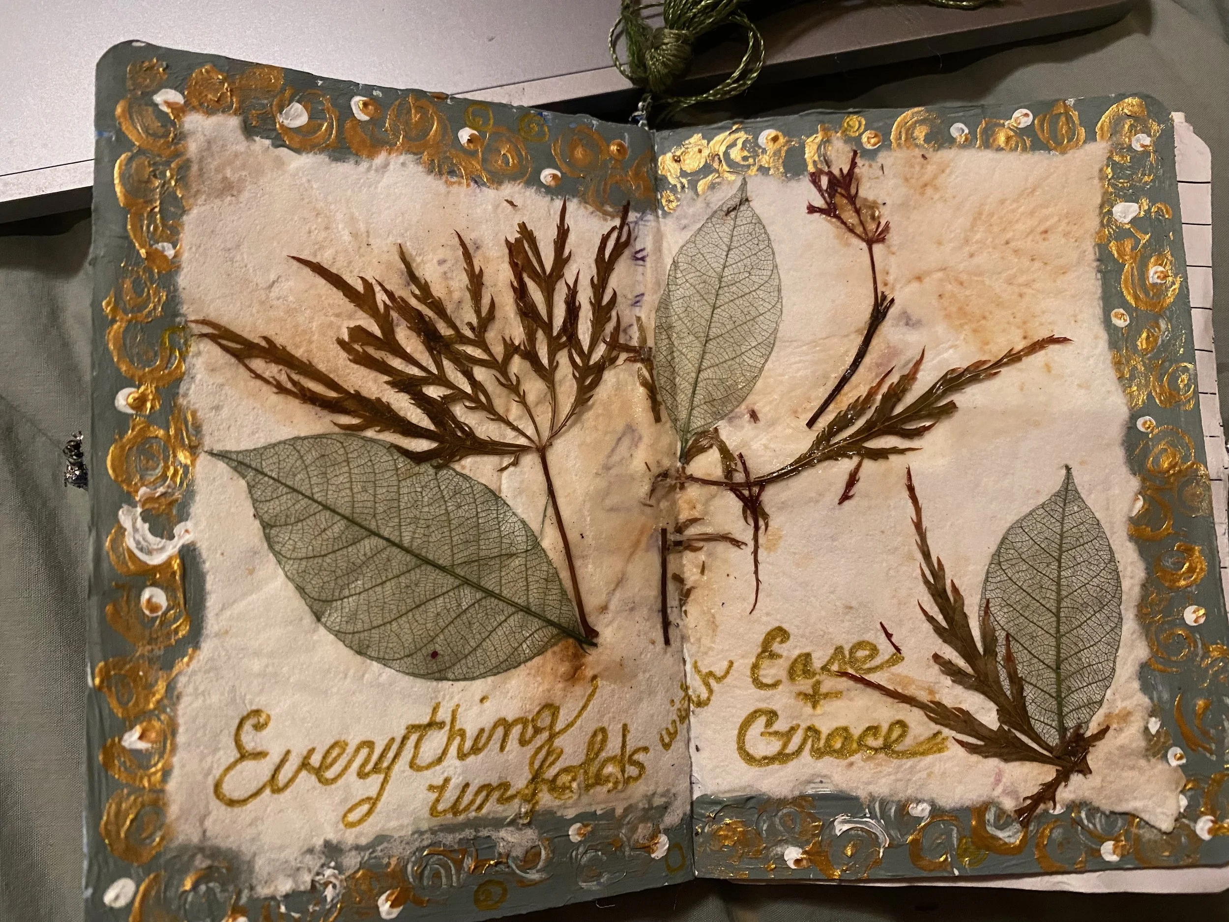 Pressed leaves and handwritten text on a decorated paper with a gold ornate border.
