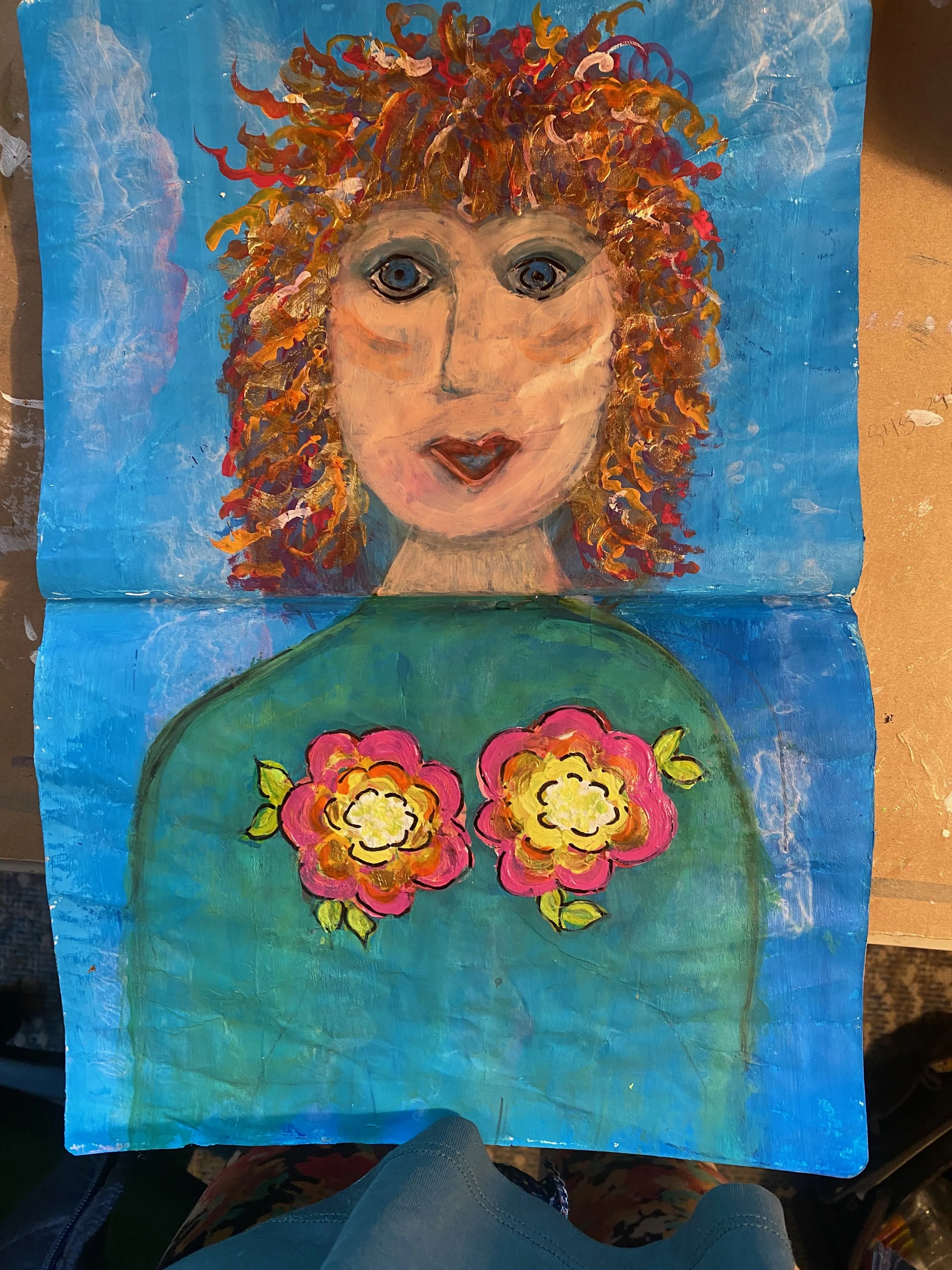 A colorful painting of a woman's face with curly hair, blue eyes, and red lipstick, set against a bright blue background with a bunch of pink and yellow flowers at the bottom.