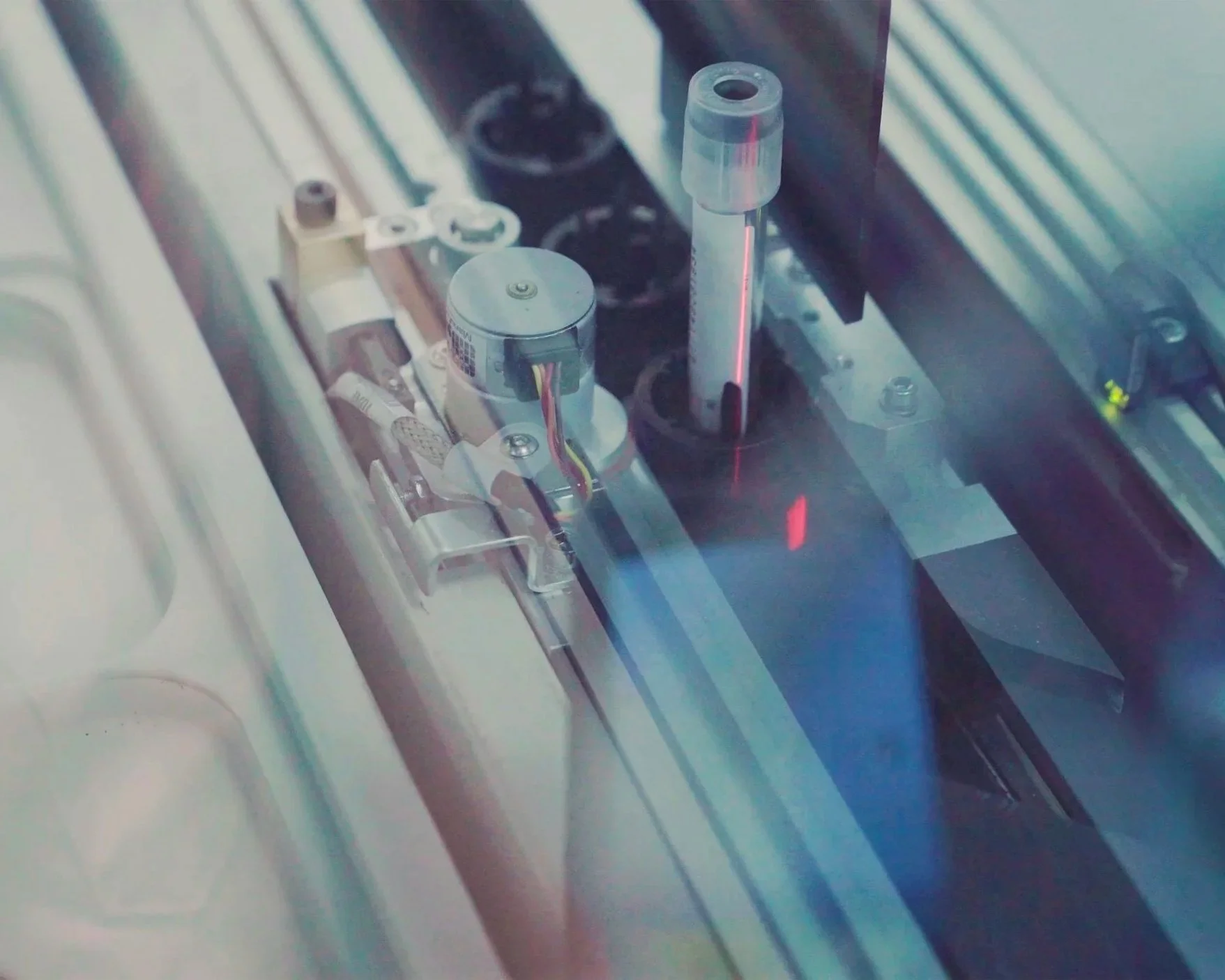 Close-up of a laser device emitting a red laser beam, with mechanical parts and components in the background.