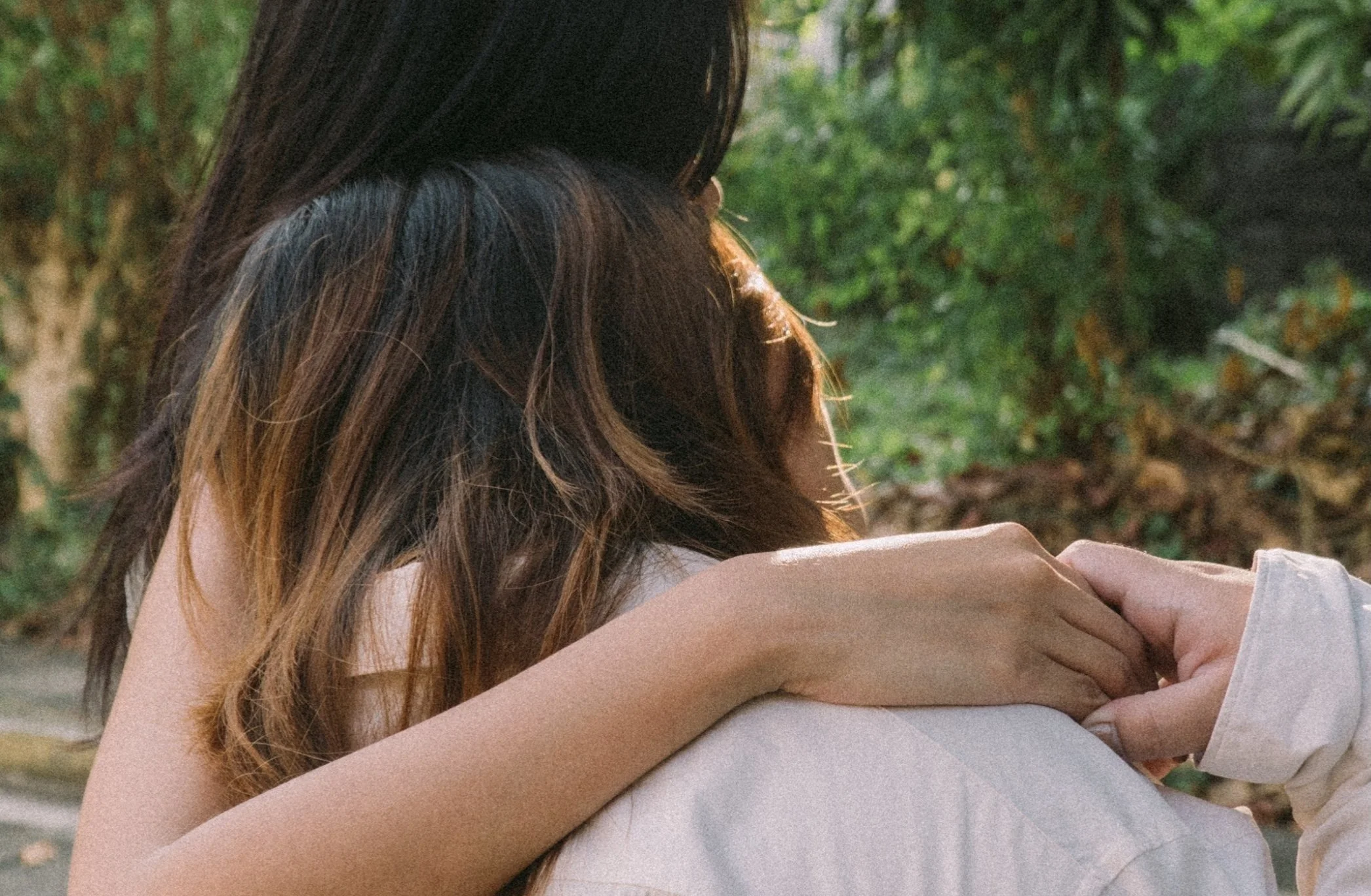 Two people embracing outdoors with a background of trees and greenery.