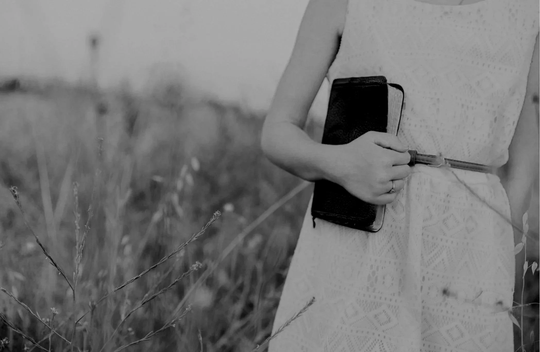 A person in a sleeveless top holding a smartphone and a syringe in a field of tall grass.