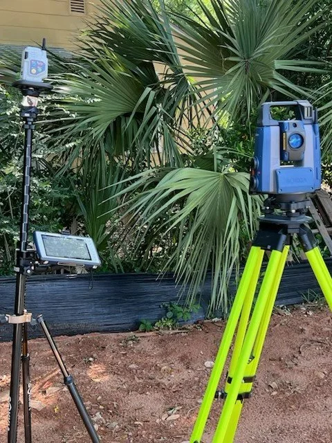 Sokkia Robotic Total Station equipment set up outdoors next to a large palm plant with green leaves.