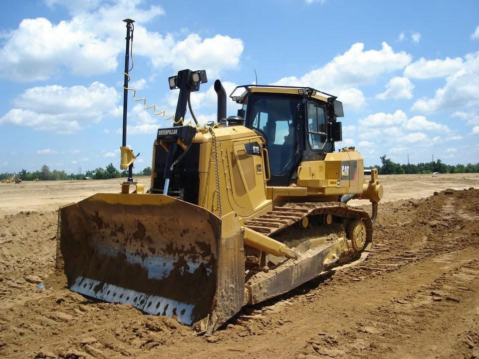 A yellow Caterpillar bulldozer working on a dirt construction site under a partly cloudy sky.