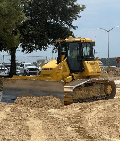 A yellow Komatsu bulldozer pushing dirt at a construction site with trees in the background.