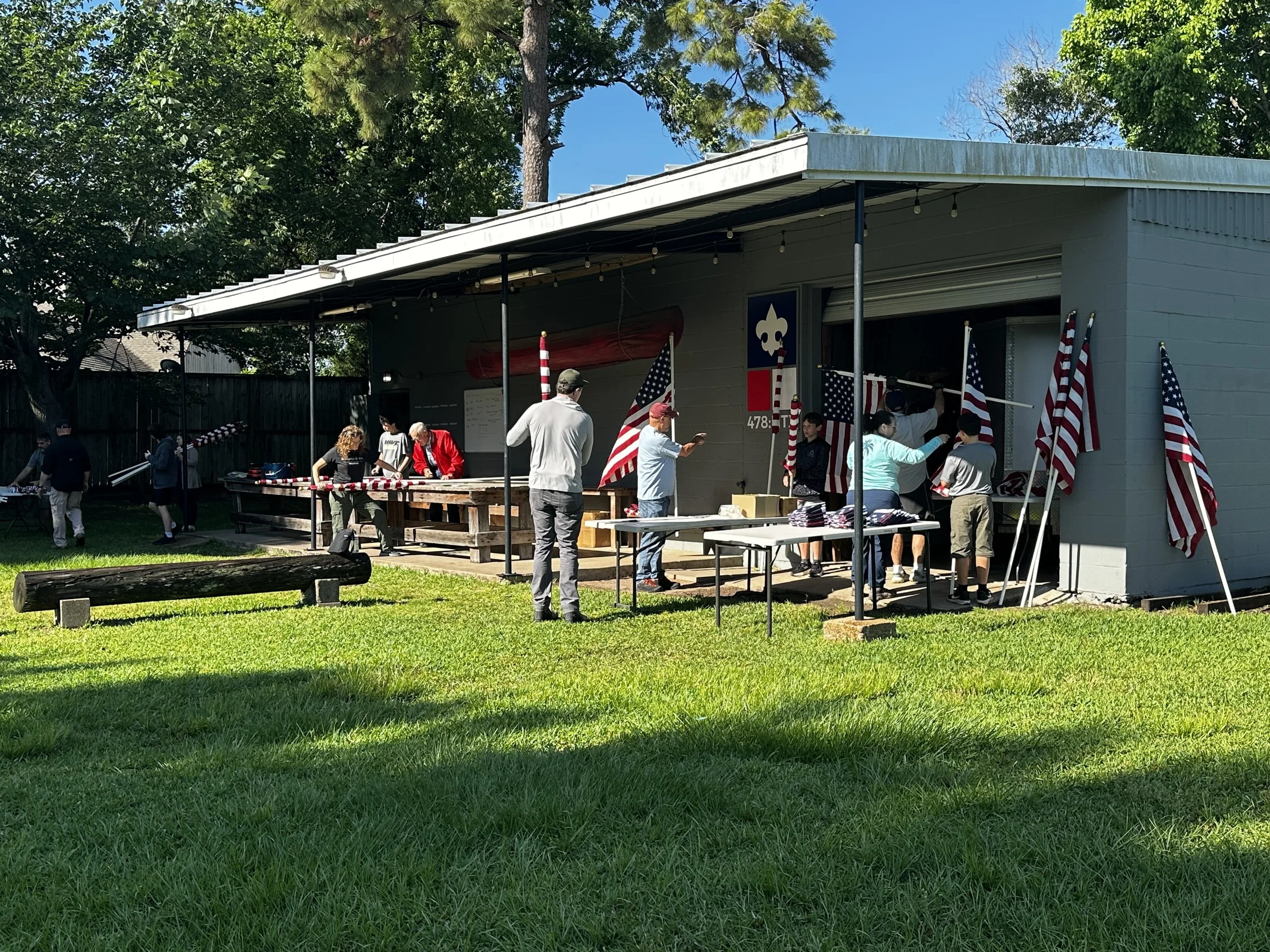 People setting up patriotic decorations outside a garage during daytime. American flags and red, white, and blue themed items are visible.
