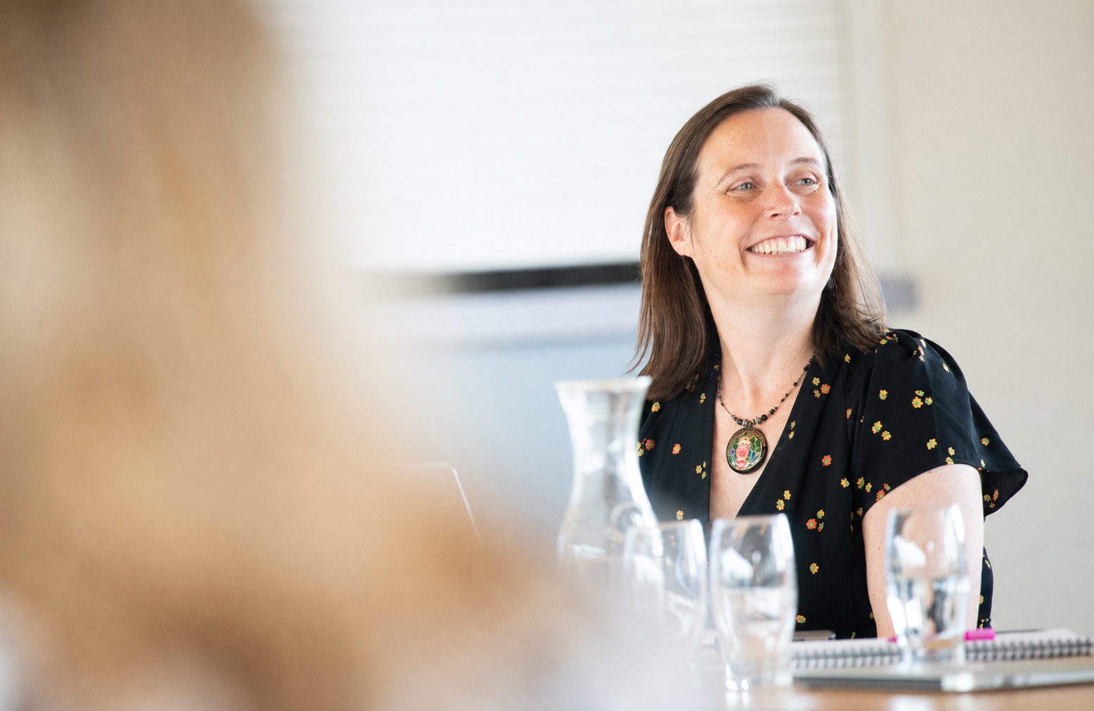 Jo Osborn, a woman, smiling in a meeting, with a glass of water in front of her