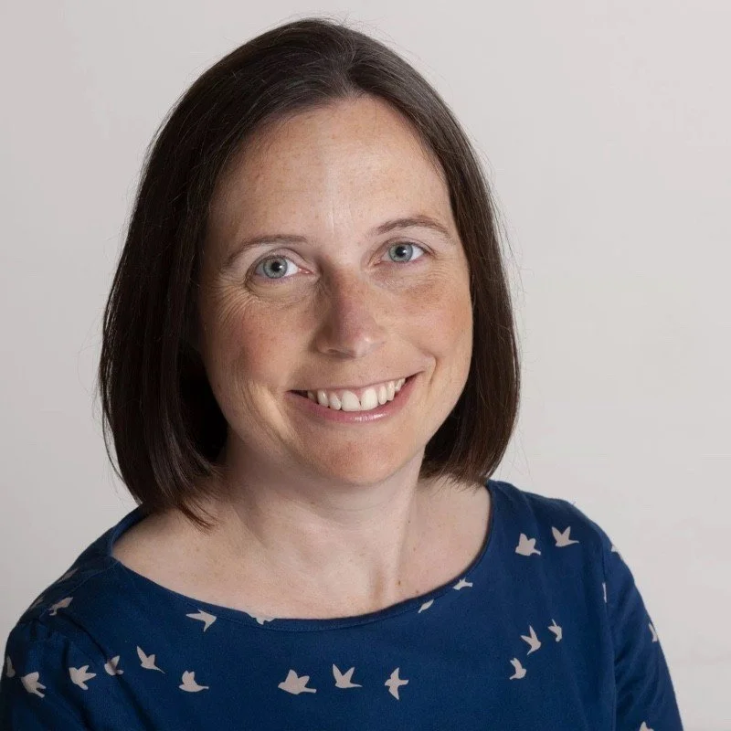 Jo Osborn - smiling woman with brown bobbed style hair and wearing a blue dress with white birds as a pattern