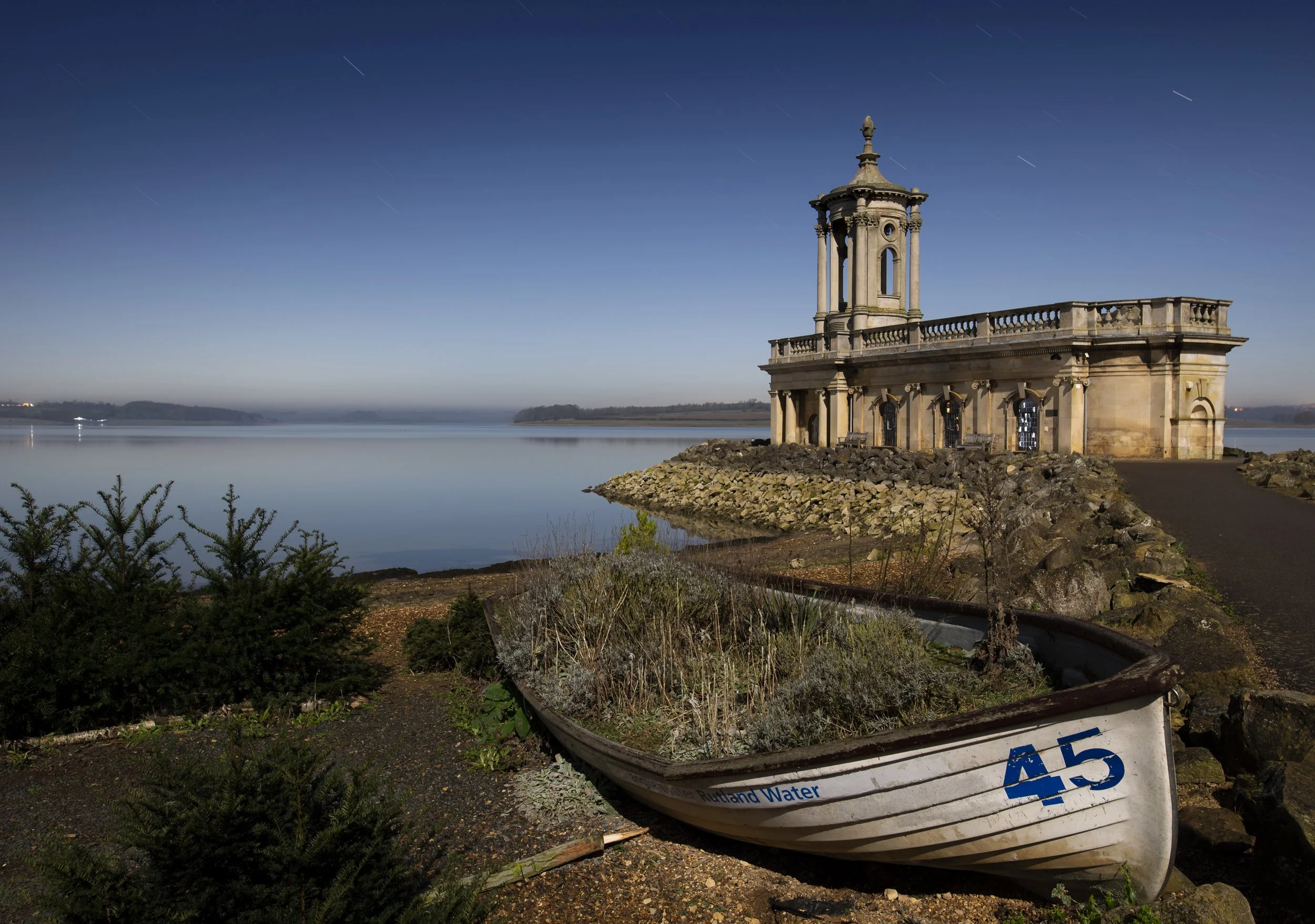 A small church sits by a lake of water with an old wooden rowing boat in the foreground