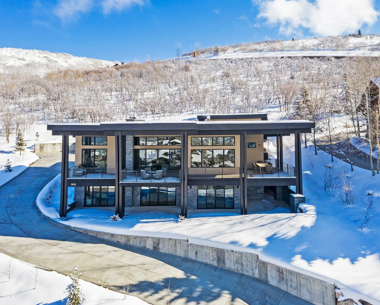 Modern two-story house with large glass windows in snowy landscape with hills and trees.