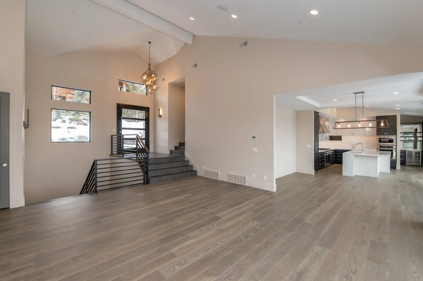 Modern open-concept living area with staircase, large windows, and kitchen featuring white cabinets, black accents, and a central island.