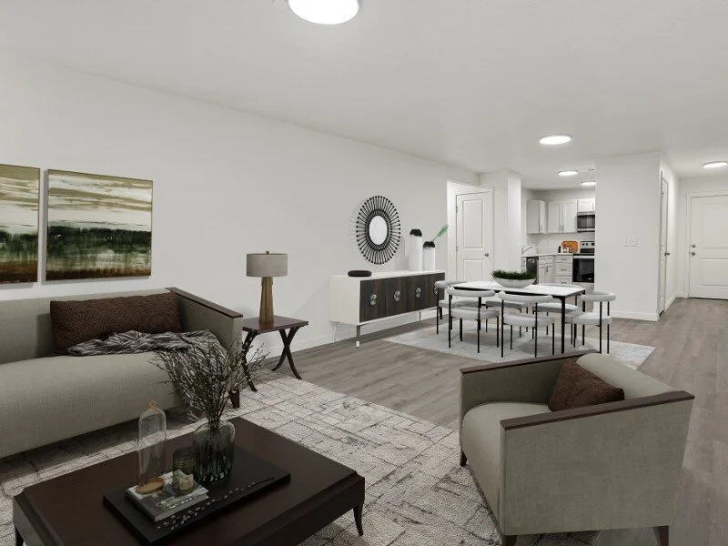 Living room with beige sofa and armchair, wooden coffee table, side table with a lamp, gray and white area rug, modern dining table and chairs, white kitchen with appliances, minimal decor, and white walls.