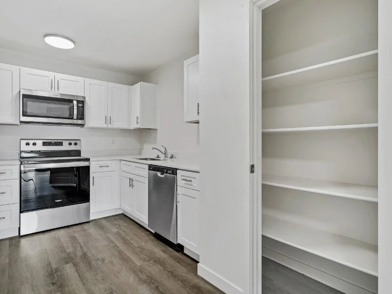 Kitchen with white cabinets, black oven, microwave, dishwasher, and empty built-in shelves.