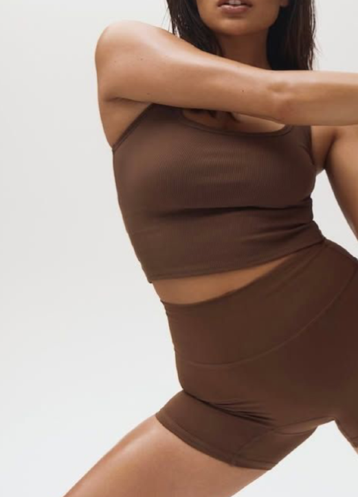 A person in a brown athletic workout outfit stretching against a plain white background.