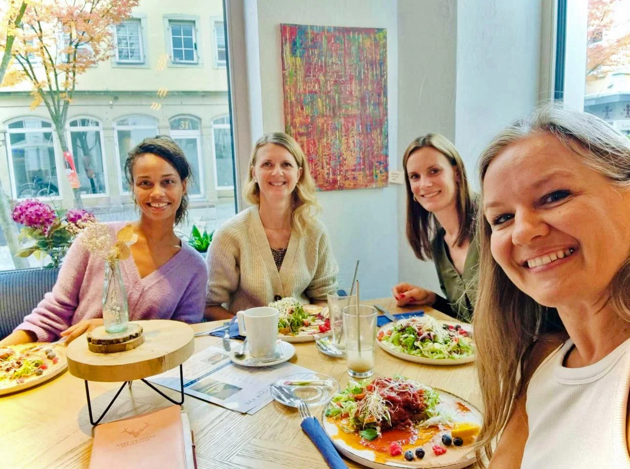 Die Frauen von growalivemoments sitzen gemeinsam am Tisch und schauen in die Kamera.
