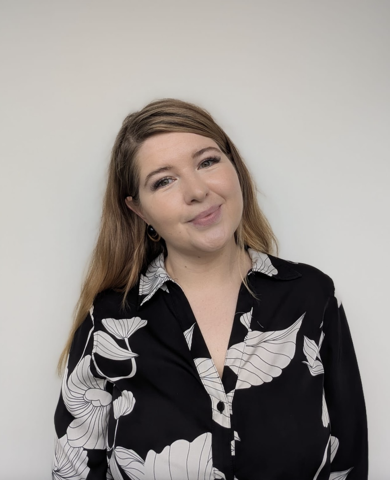 Elizabeth Demine smiling at the camera, wearing a black blouse with a white floral pattern against a light grey background.