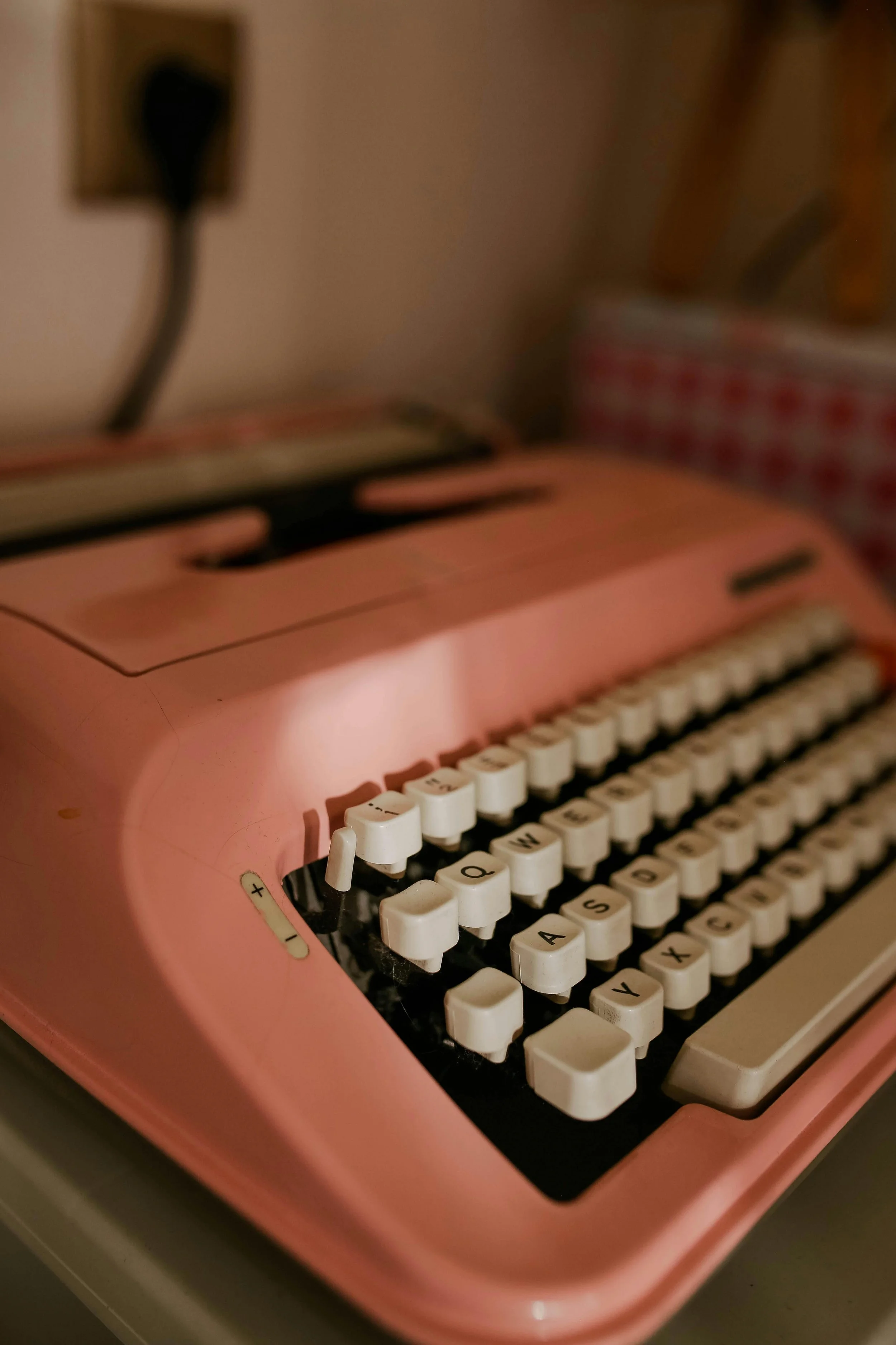A pink vintage typewriter with white keys on a desk, with a blurred background.