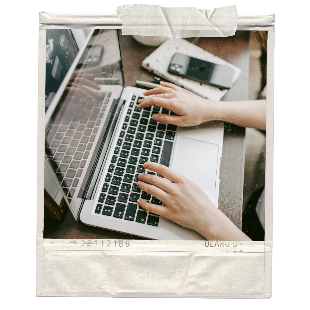 Hands typing on a laptop keyboard with a smartphone and a notebook on the desk.