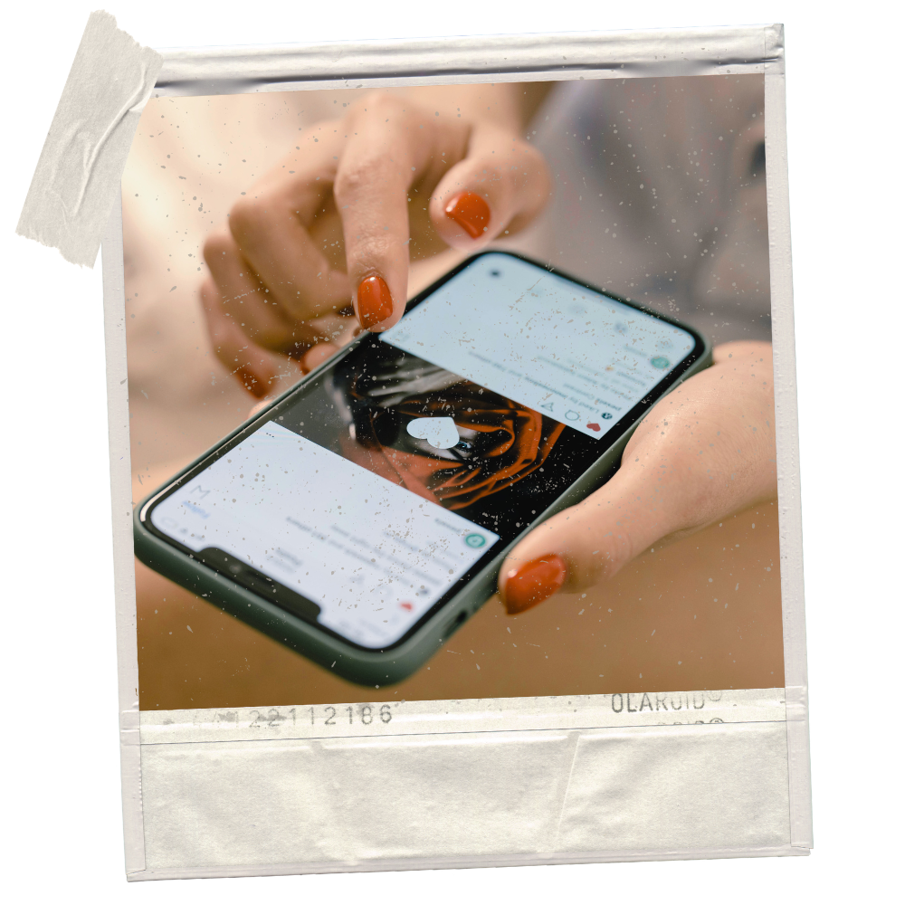 Person with orange painted nails holding a smartphone, viewing a social media app with a heart symbol, on a polaroid-style photo with a vintage effect.