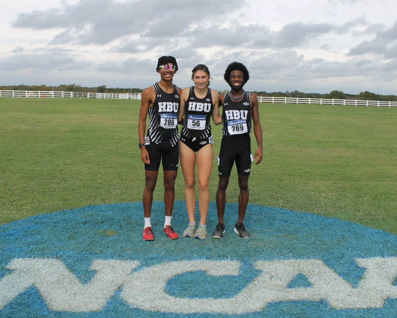 Justice, Jessica, and Travis standing on the NCAA logo at the South Central Regionals for cross county. Justice and Travis raced a 10k and Jessica raced a 6k. All 3 athletes, now coaches, raced with true grit.