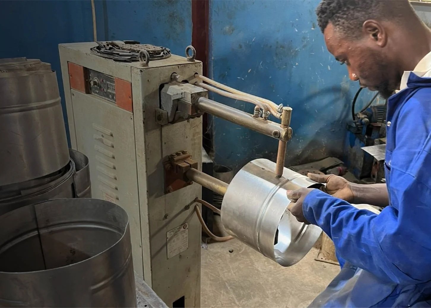 A man operating a metal sheet rolling machine in a workshop.