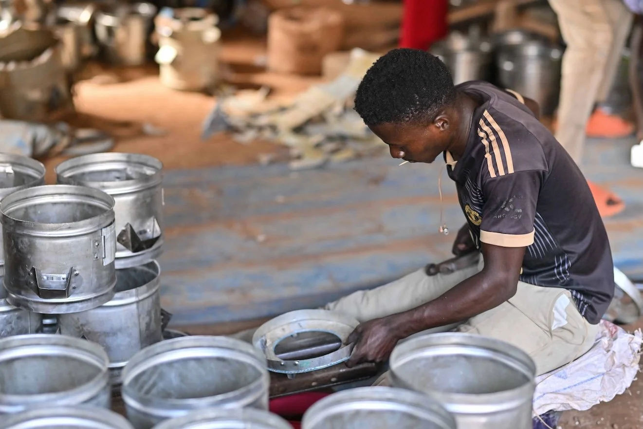 A young man working on a metal object surrounded by several metal containers in a workshop.