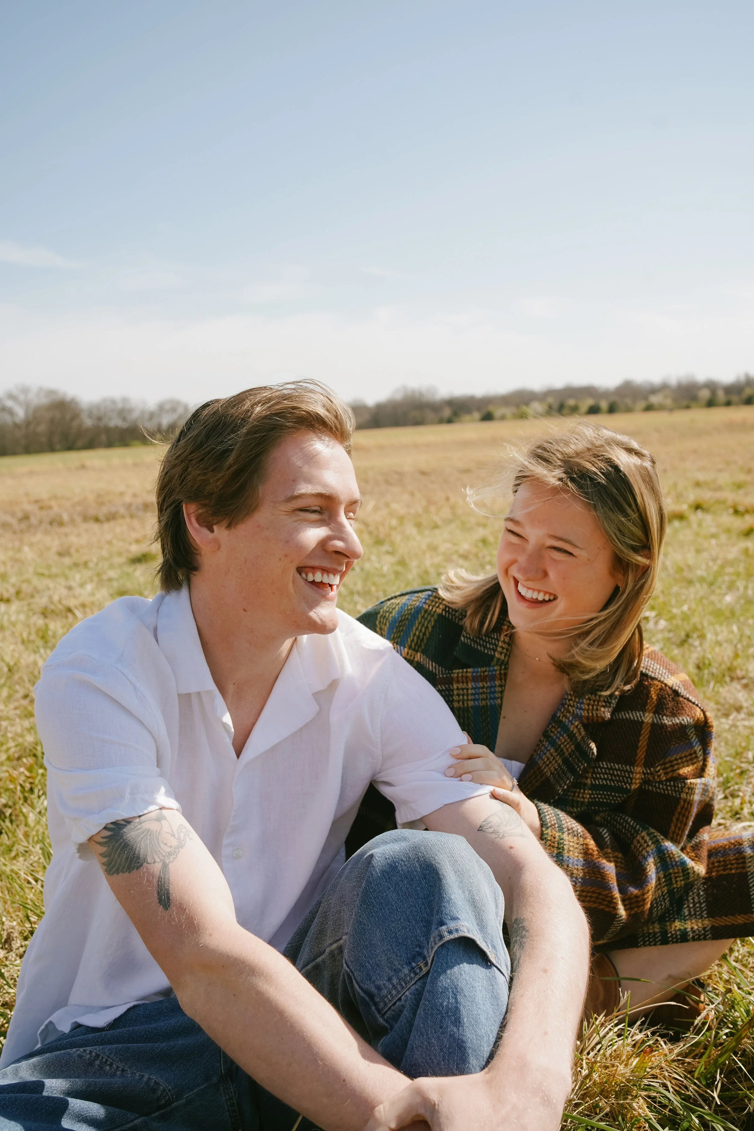 A young man and woman sitting on the grass in a field, smiling and enjoying each other's company on a sunny day.
