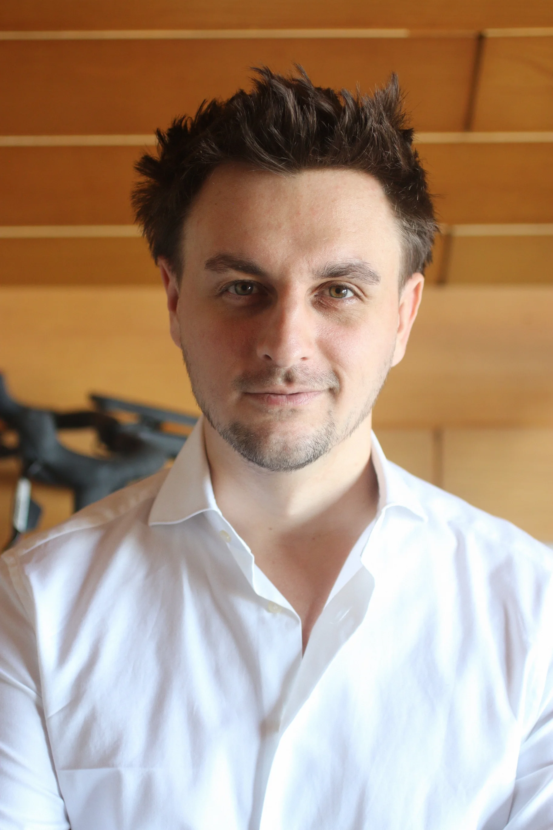 Portrait von Lukas, dem Gründer & Designer hinter FUXSTUDIO, in einem weißen Hemd vor einer Holzdecke, Blick halb zur Kamera, lächelnd.