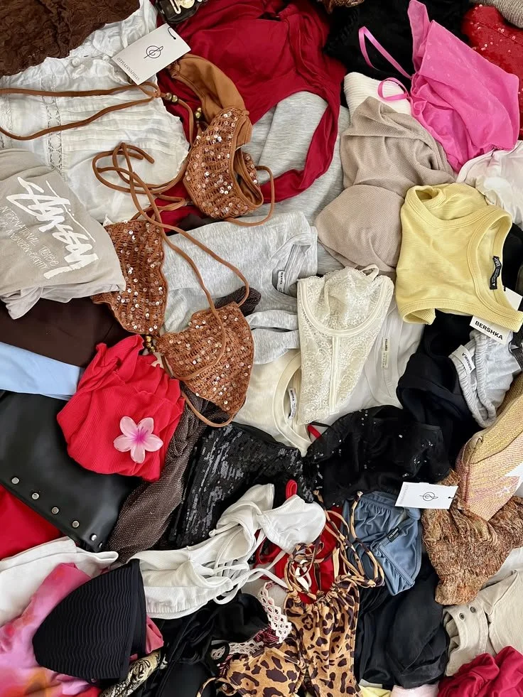 A pile of various women's clothing and accessories, including bras, tank tops, and skirts, with some tags attached.