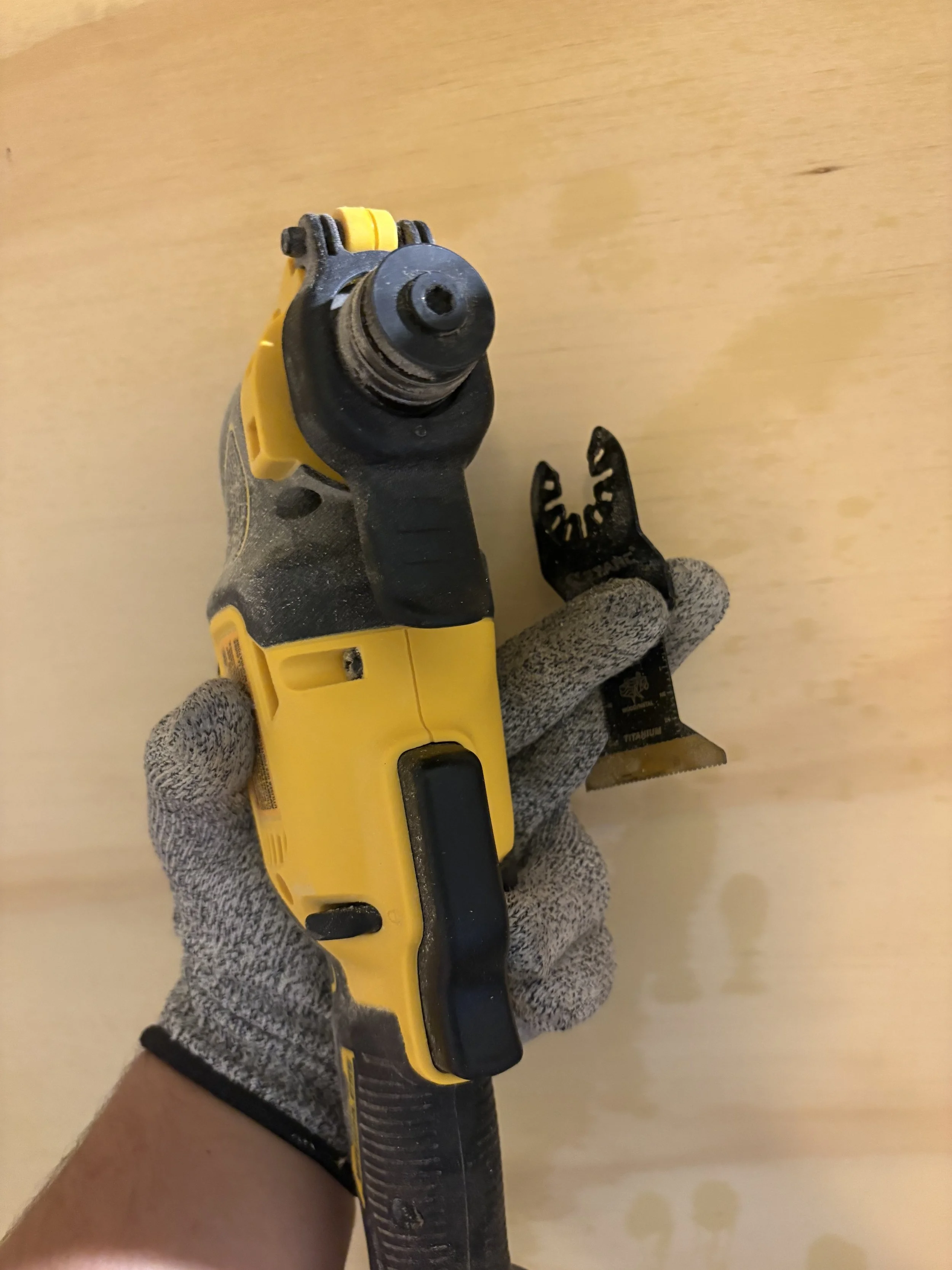 Close-up of a person wearing gray gloves holding a yellow and black cordless power drill with the drill bit attached.
