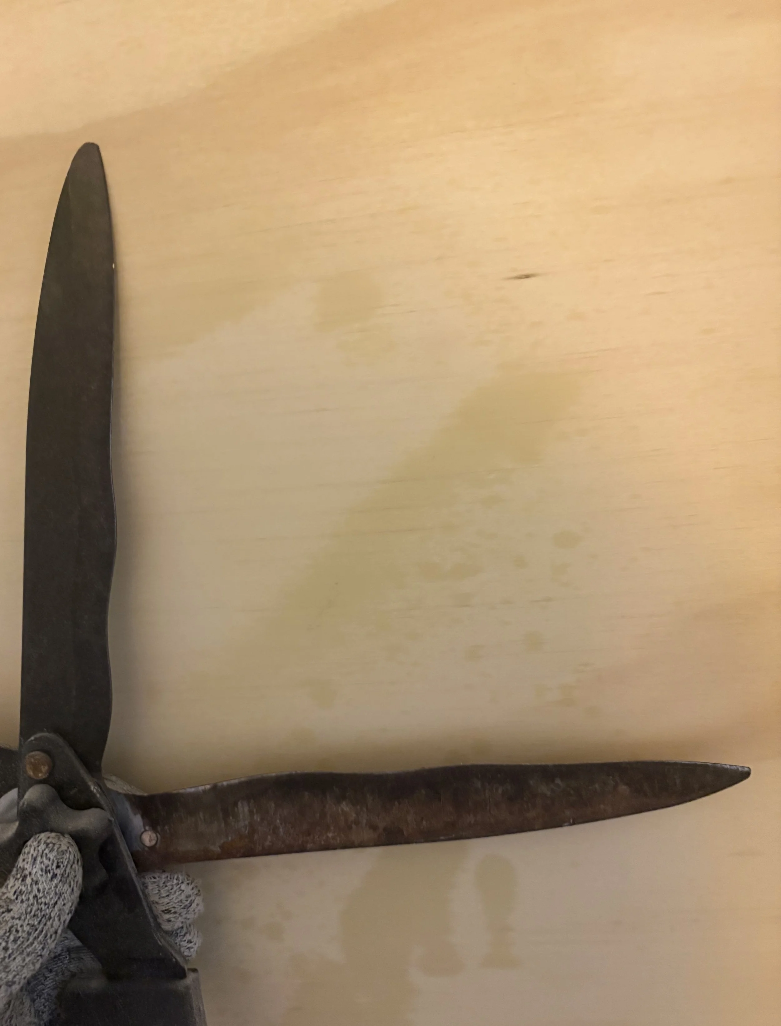 A metal crowbar or pry bar resting on a light-colored wooden surface, with the handle partially obscured by a person's foot wearing patterned socks and black shoe.