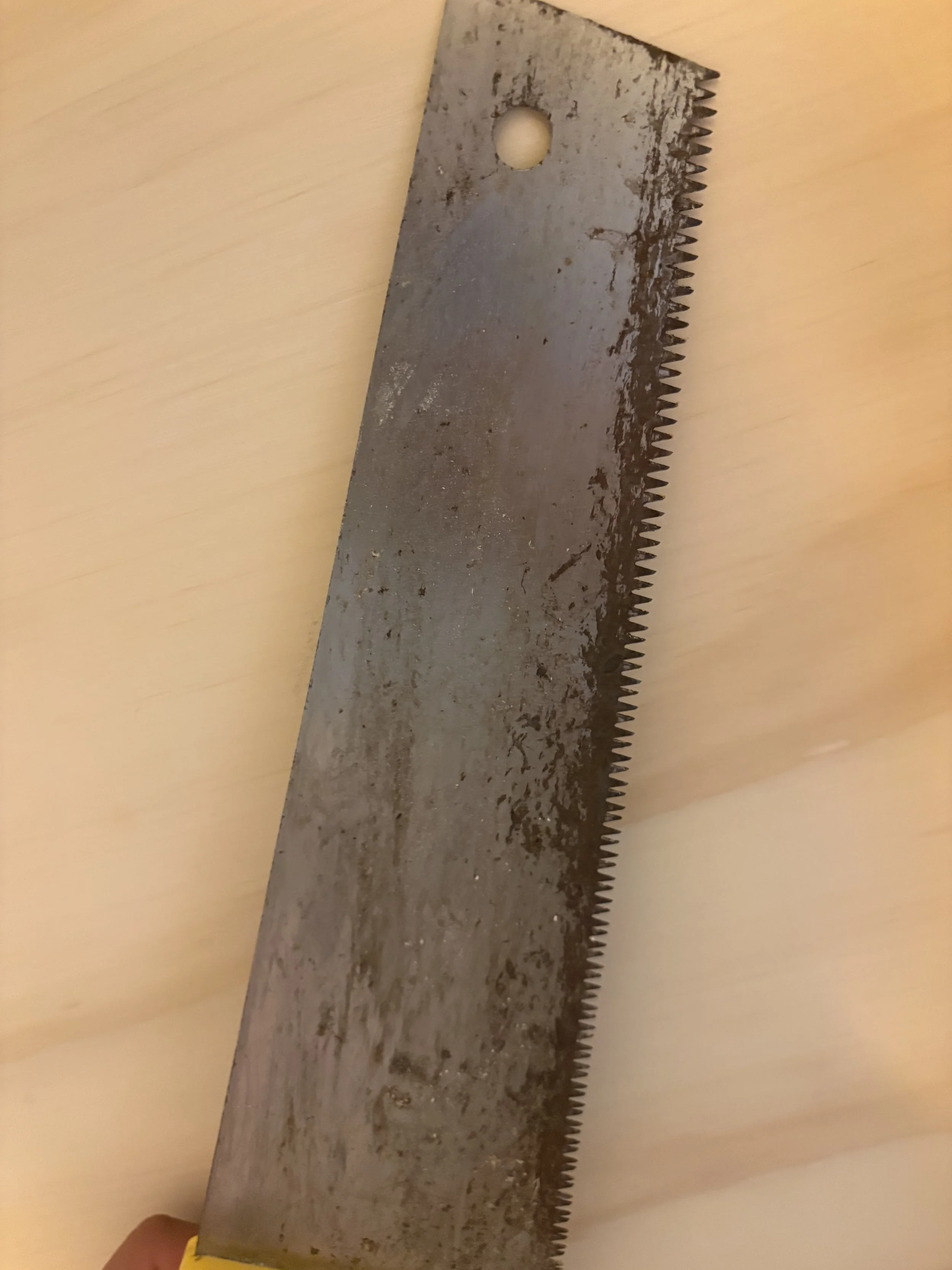 A close-up photo of a rusty hacksaw blade lying on a wooden surface.