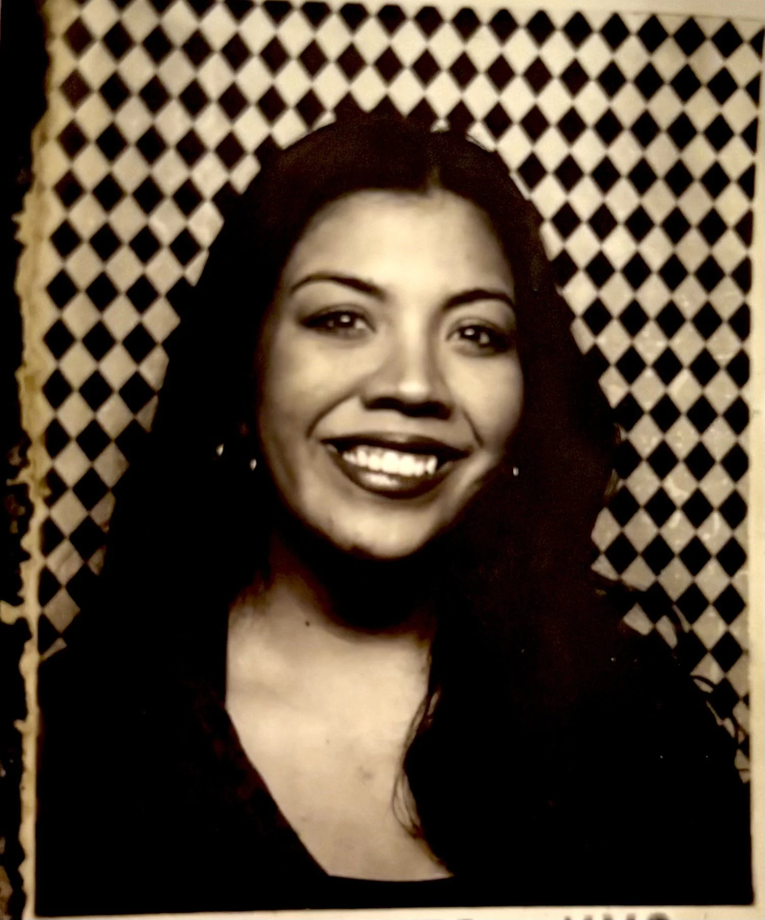 Black and white portrait of a woman with long dark hair, smiling, in front of a patterned background.