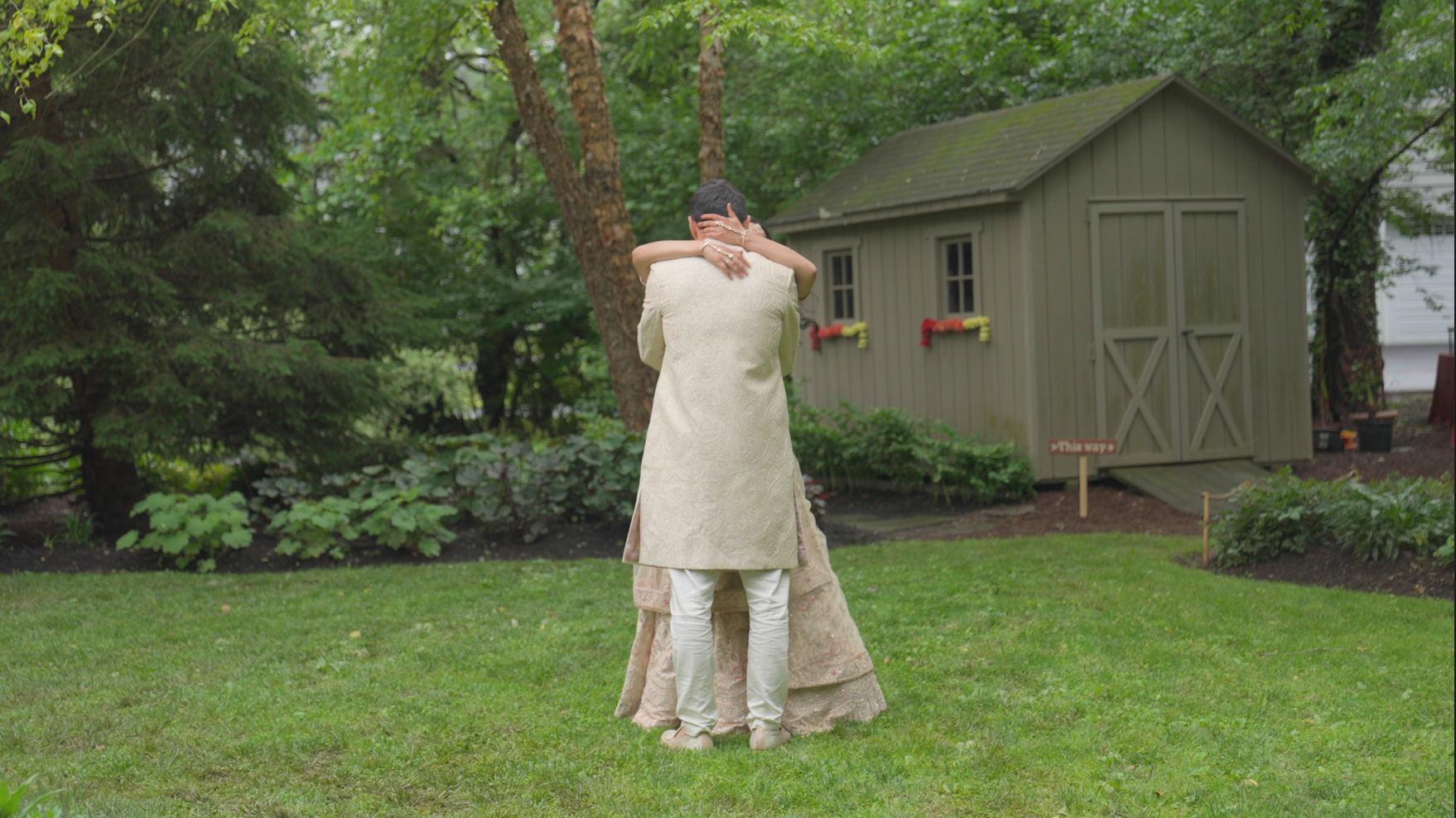 A couple dancing outdoors on a lawn with a garden shed in the background, surrounded by trees and greenery.