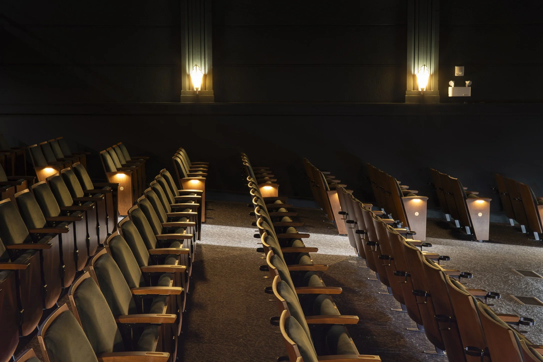 Rows of theater seats, dim lighting, and wall sconces illuminating the dark walls.