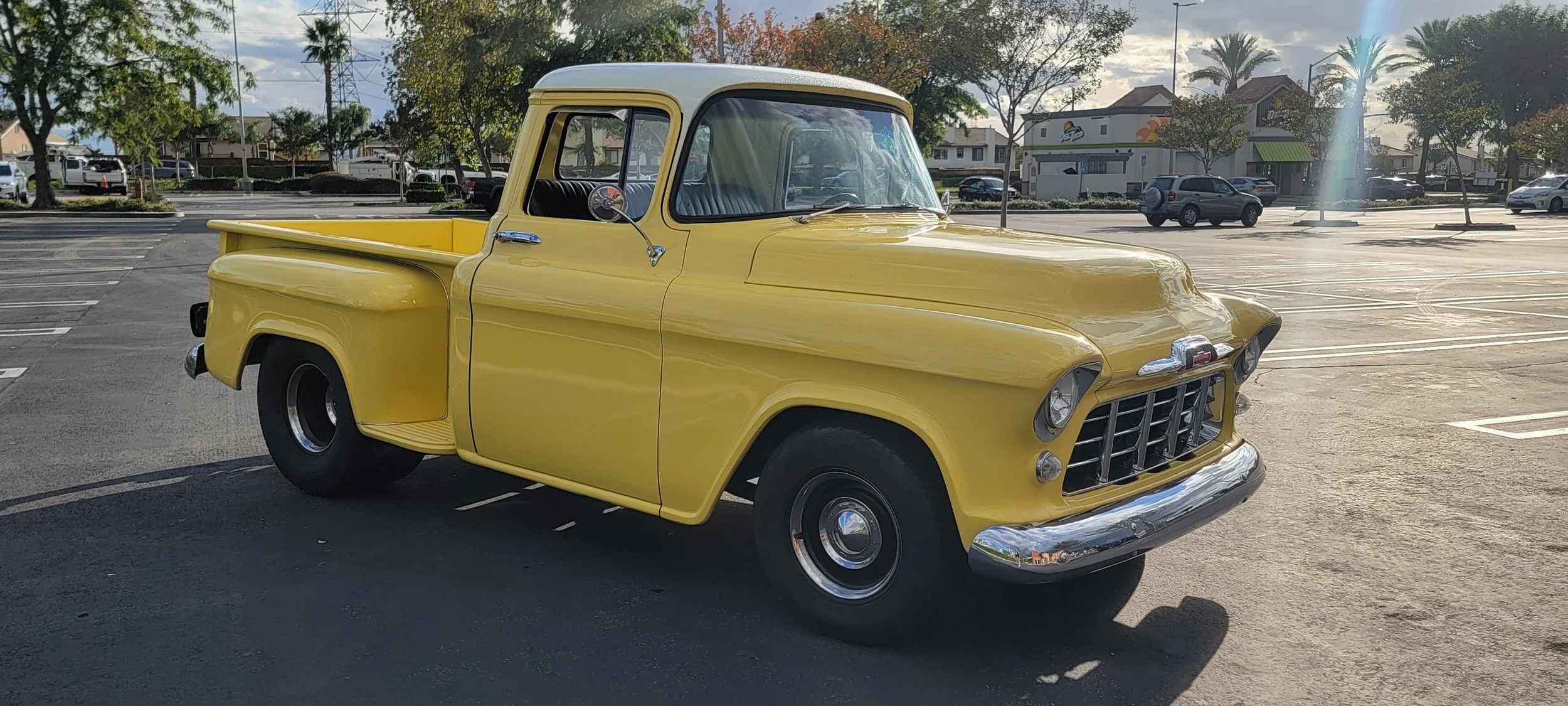 A yellow vintage pickup truck parked in an outdoor parking lot.