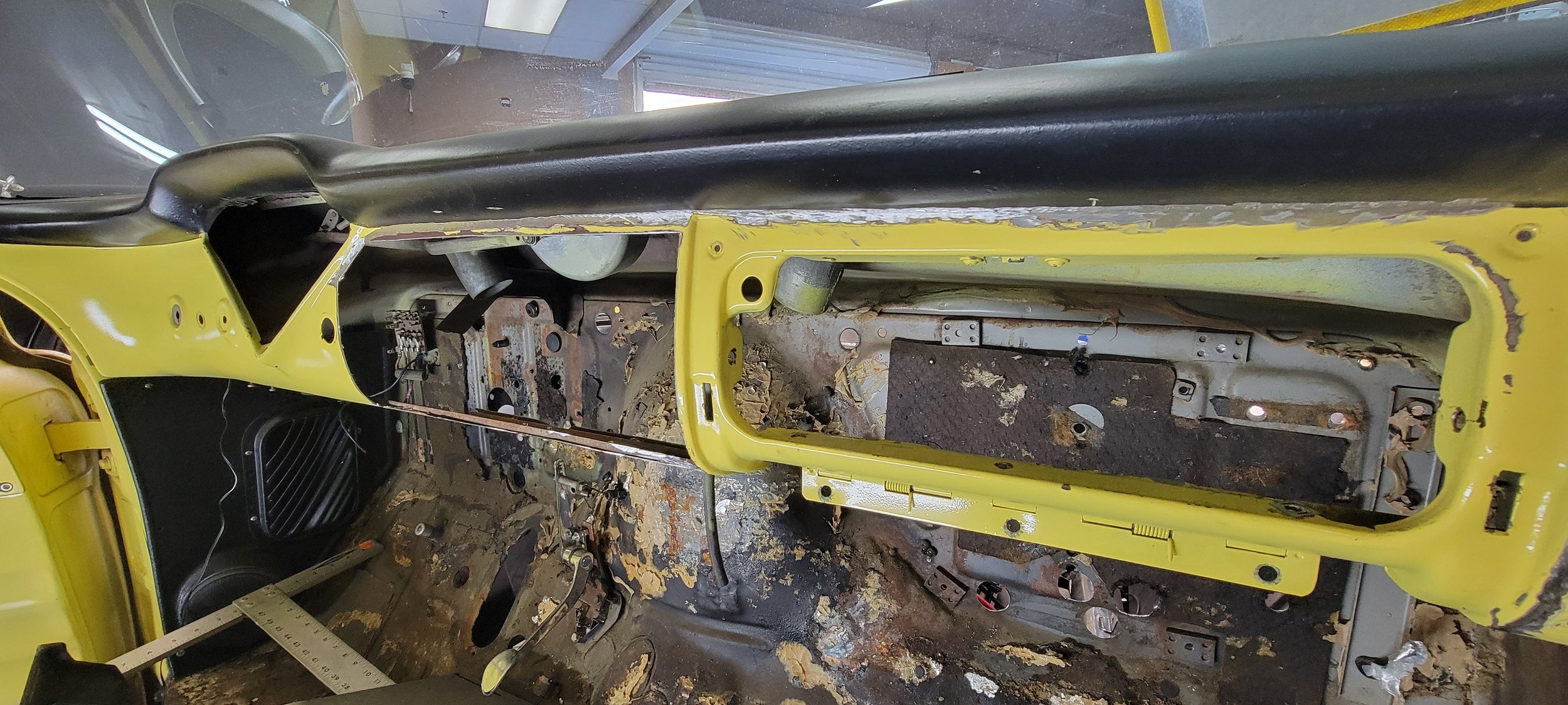 Interior of a stripped car with yellow door frames, rusted floor, missing seats, and exposed wires.