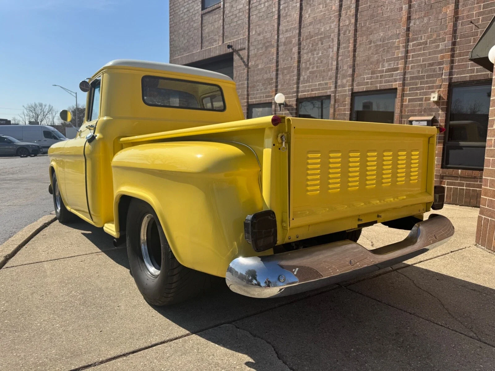 Yellow vintage pickup truck parked on sidewalk near brick building.