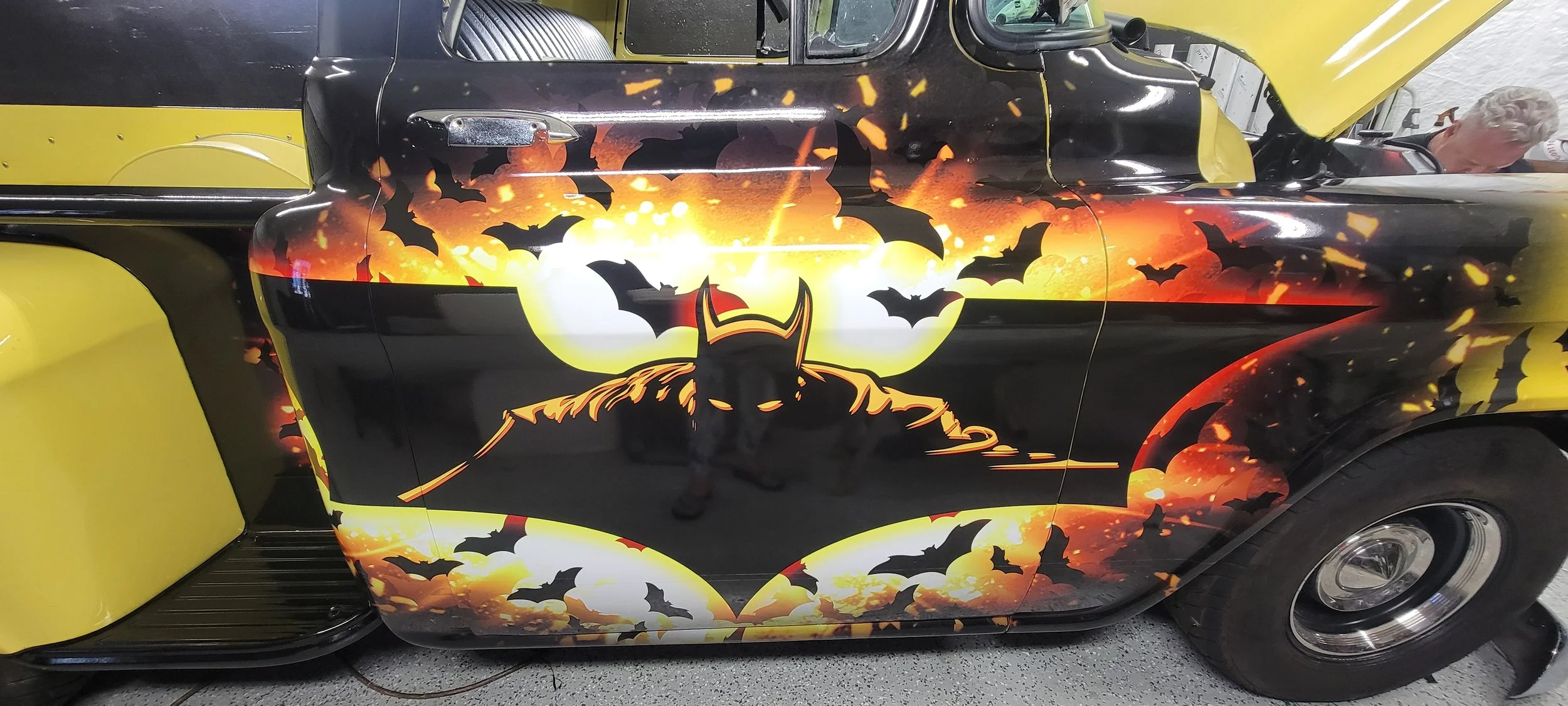 A custom car with Batman-themed artwork featuring bats, a sunset, and Batman's mask on the side.