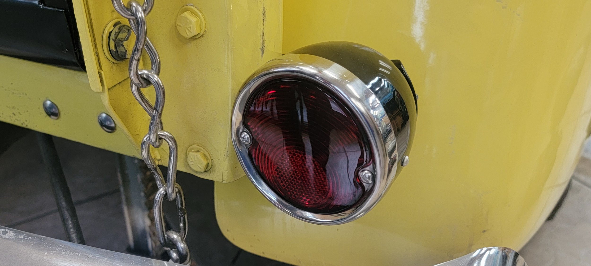 Close-up of a yellow vehicle with a red tail light, secured with a metal chain and bolts.