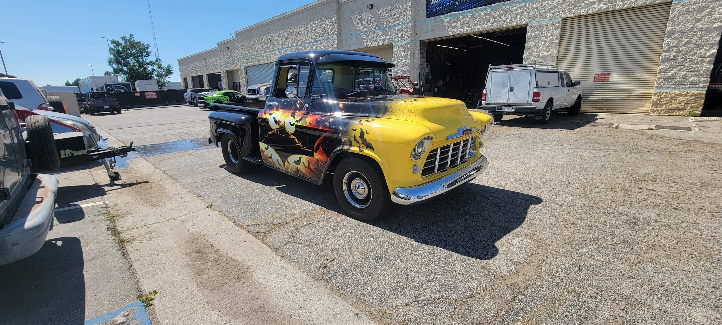 A vintage pickup truck with a custom Halloween-themed paint job featuring bats, a pumpkin, and a haunted house scene parked outside a building.