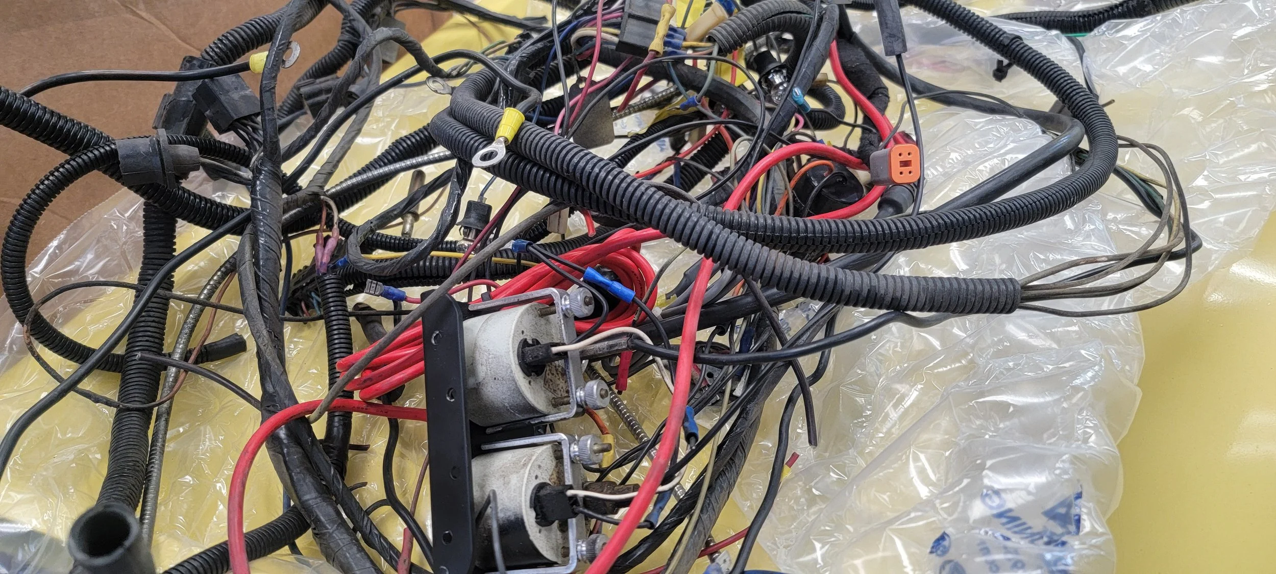A tangled mess of electrical wires and cables, some with connectors, resting on a yellow plastic sheet.