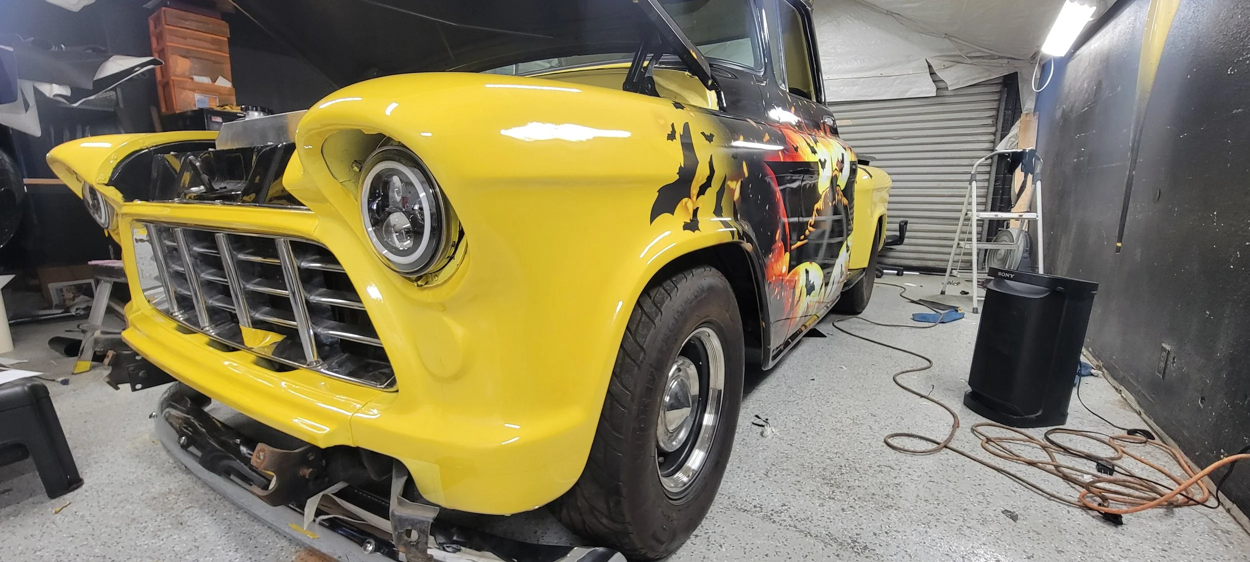 Yellow vintage car with Halloween-themed bat and pumpkin decals in a garage.