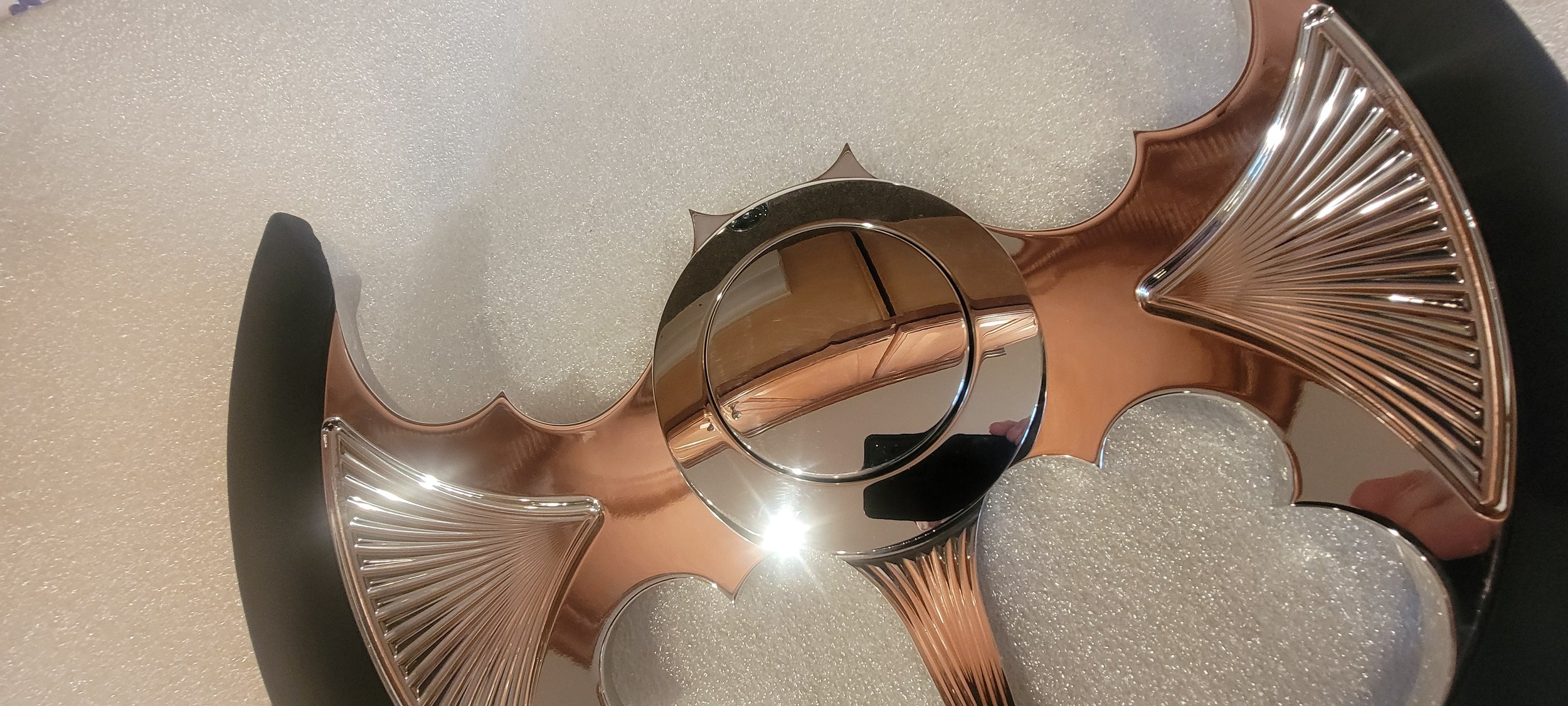 A decorative metallic object with curved, claw-like extensions and a central hollow ring, displayed on a textured surface.