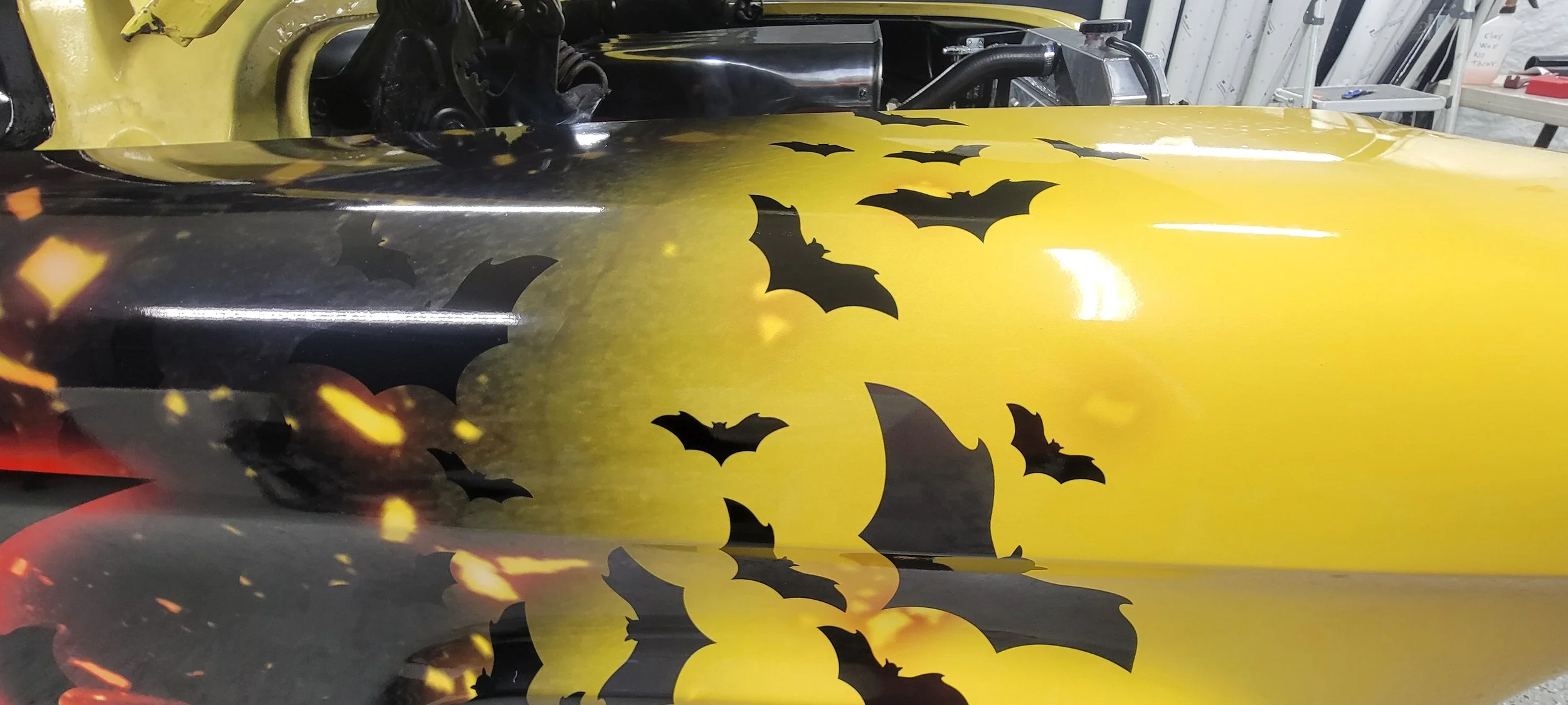 Close-up of a yellow surface with black bat-shaped decals and a black engine part in the background.