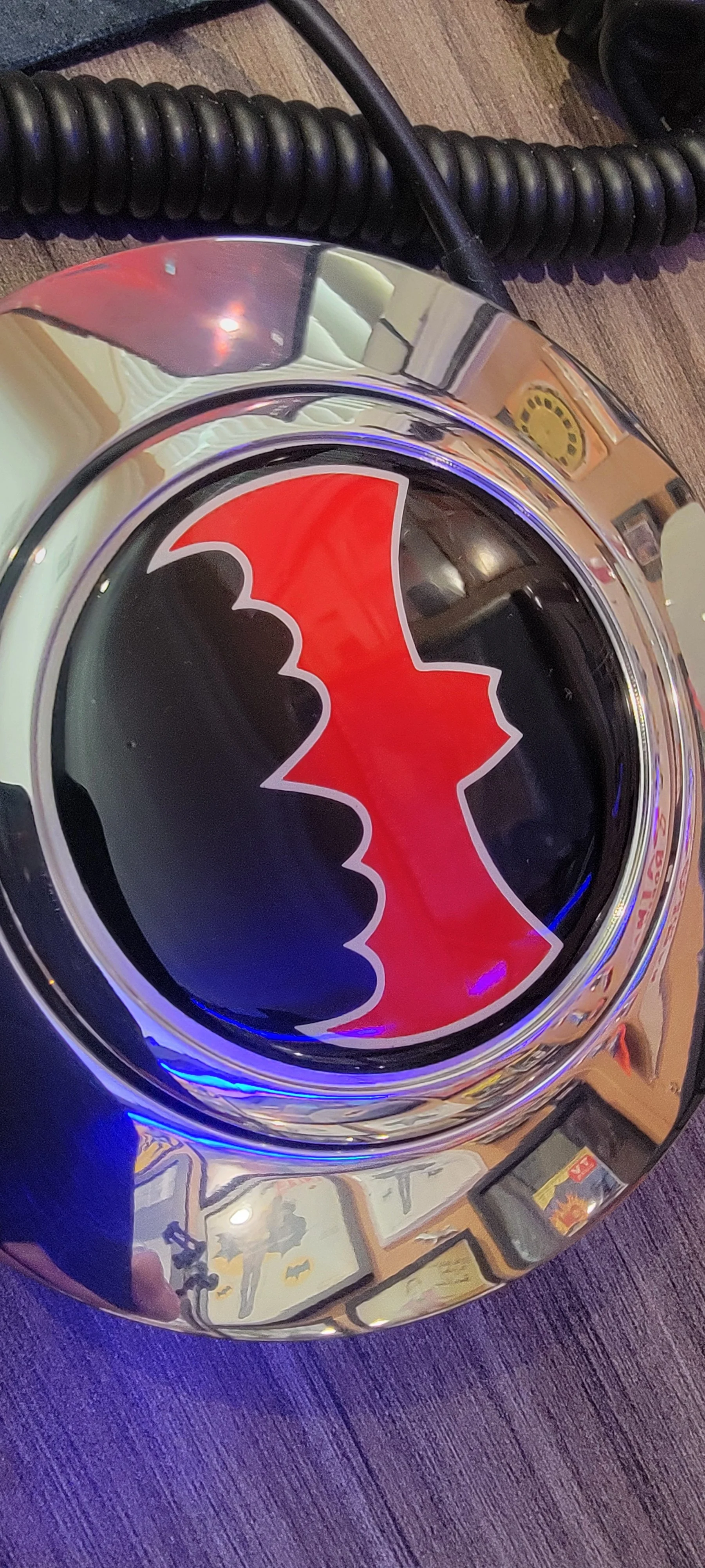 A chrome surface with a stylized red and black dragon logo, reflecting the surrounding framed pictures on the wall and a person's hand holding a camera.