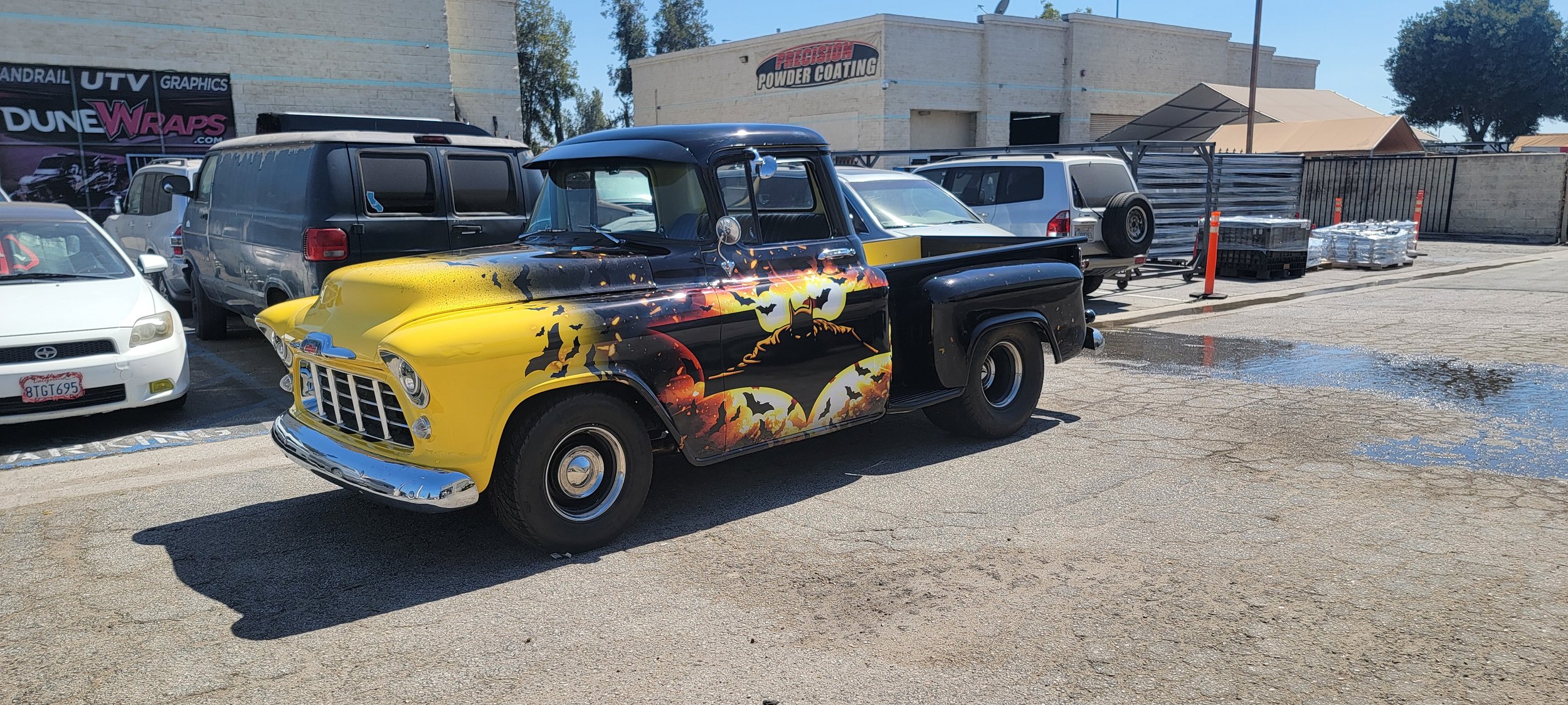 A vintage black and yellow truck with a Halloween-themed Batman mural parked in a lot.