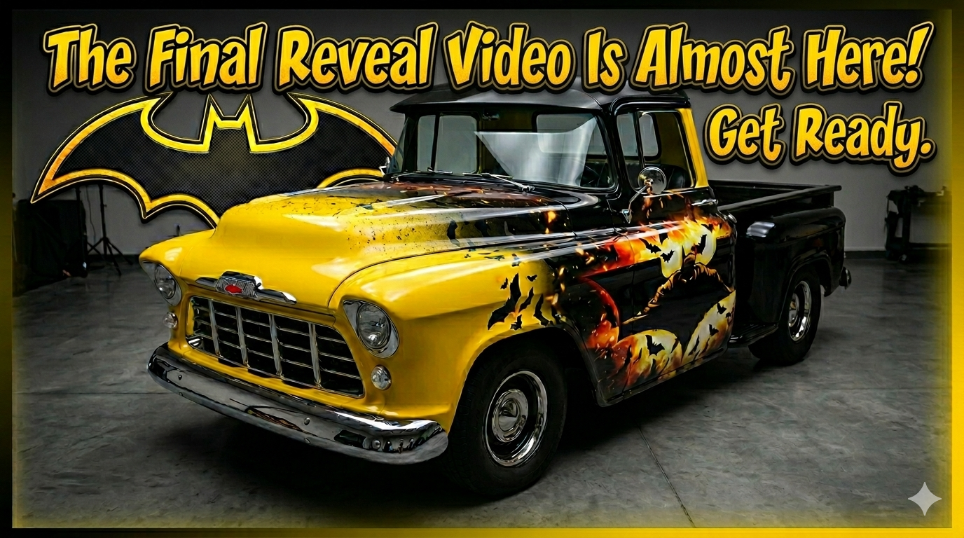 A vintage Chevrolet truck with yellow and black paint featuring a Halloween-themed design with bats and a pumpkin, parked indoors with a large Batman logo and promotional text in the background.