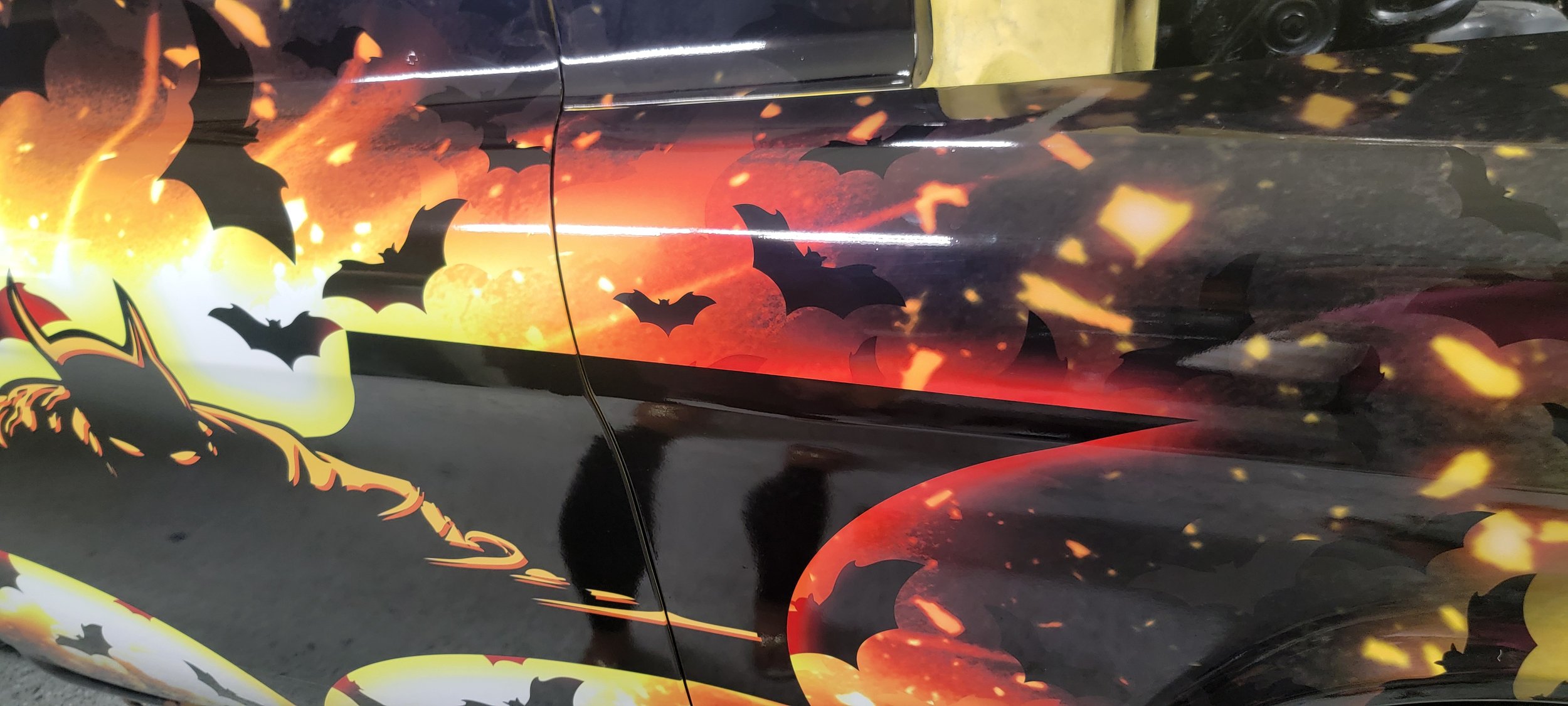 Car with Halloween-themed paint design showing flying bats, orange and yellow flames, and a witch's hat on the left side.
