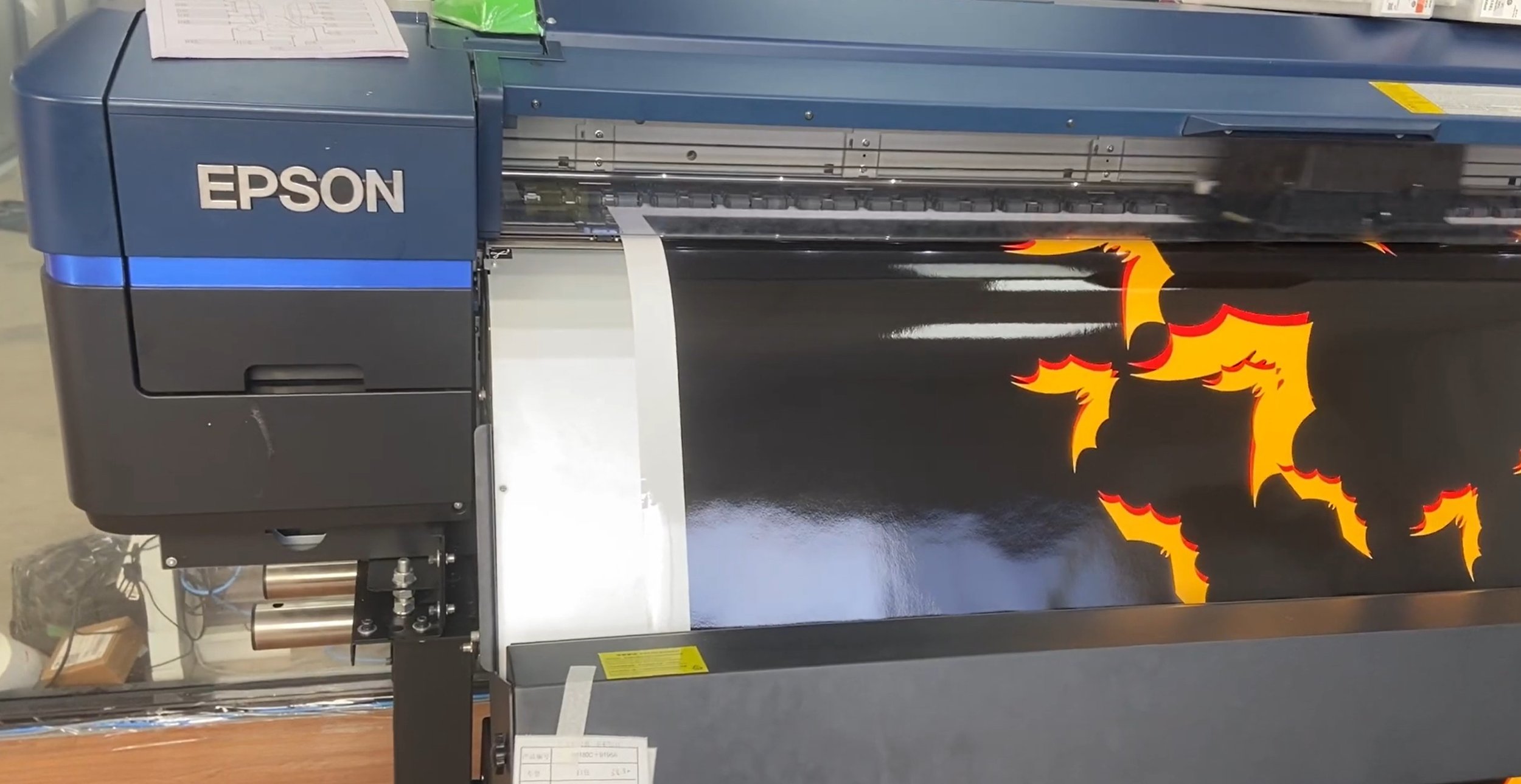 A large Epson printer printing a design of flames with orange, red, and yellow colors.