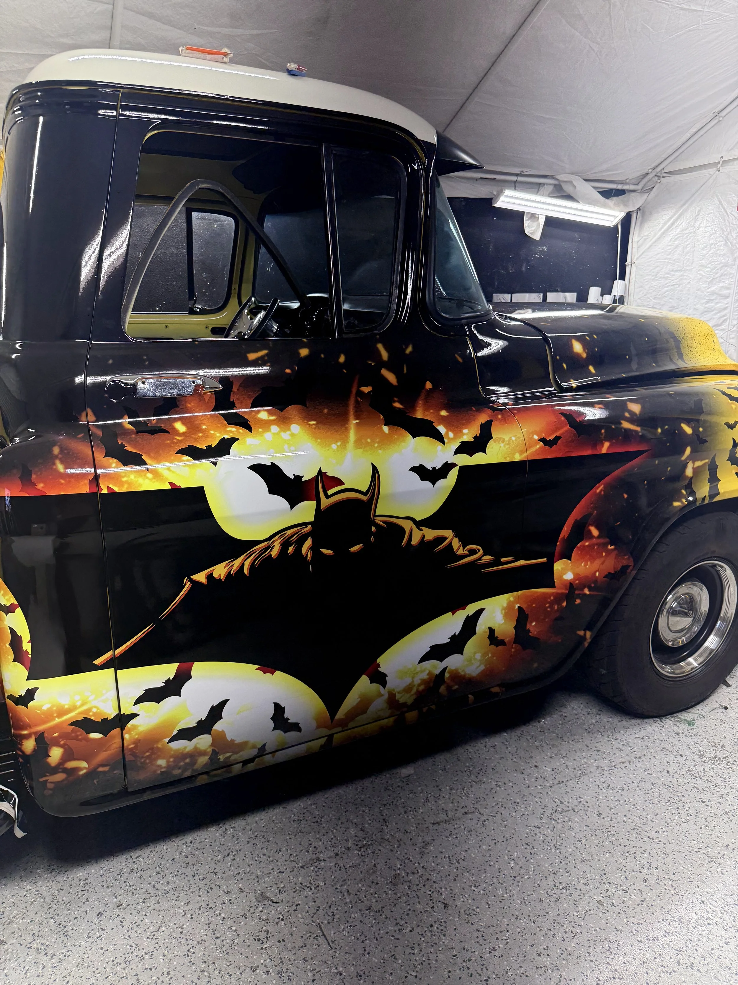 A vintage black car featuring a Batman-themed design with bats flying across a yellow, orange, and black background.